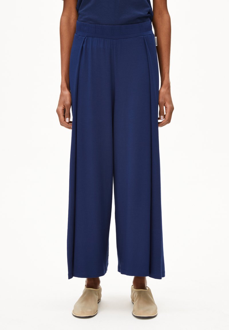 Marineblauwe wijde broek van zacht materiaal met een elastische tailleband en voorplooien. Soepele textuur met een vloeiende silhouet.