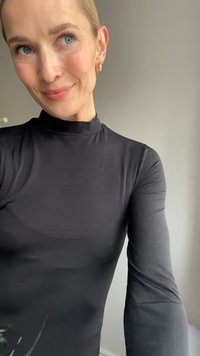 Crna majica dugih rukava s visokim ovratnikom, napravljena od glatkog, priljubljenog materijala, s diskretnim cvjetnim uzorkom u donjem kutu.