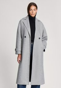 Szary wełniany płaszcz z podw ójnym zapięciem, szerokimi klapami i zapinanymi mankietami. Nosi się go na czarnym golfie i dżinsach. Gładka faktura.