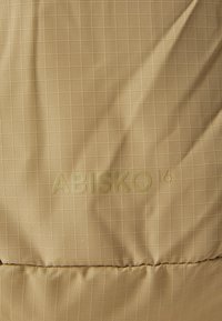 Textured yellow-brown fabric with a grid pattern, featuring embossed "ABISKO 14" branding, showcasing smooth and durable construction.