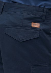 Παντελόνια ναυτικού μπλε χρώματος με λοξή πίσω τσέπη που διαθέτει ένα καφέ δερμάτινο σήμα της μάρκας Timberland πάνω από την τσέπη.