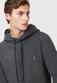 Dunkelgrauer Hoodie mit weicher Textur, ausgestattet mit einer Kapuze mit Kordelzug und einem kleinen, in zartem Rosa gestickten Logo auf der Brust.