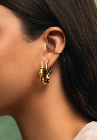 Pendientes de aro en oro y plata con un diseño texturizado. El pendiente de oro presenta una forma inspirada en el bambú, mientras que el de plata tiene un acento elegante.