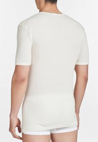 T-shirt bianca a maniche corte realizzata in tessuto morbido, con colletto rotondo e una superficie liscia. La maglietta è aderente e arriva fino alla vita.