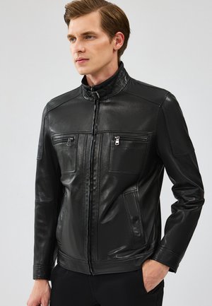 Chaqueta de cuero negro con un alto cuello, frente con cremallera y dos bolsillos en el pecho. El diseño es ajustado con una textura suave y brillante.