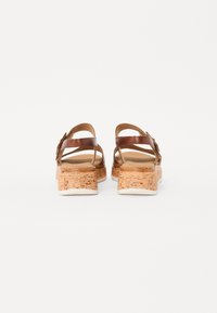 Brown leather sandals with cork wedge heels and white outsoles. Multiple straps crisscross over the back, providing an open design.