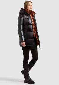 Zwarte pufferjas met een glanzende afwerking, voorzien van een capuchon, ritssluitingen en een bruine binnenlaag. Draag dit over een donkere gebreide rok en zwarte laarzen.