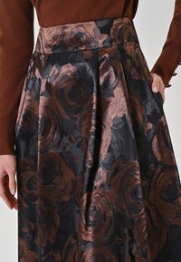 Schwarzer Rock mit einem filigranen braunen Rosenmuster, hergestellt aus glattem, strukturiertem Stoff. Besitzt eine taillierte Passform und ein plissiertes Design.