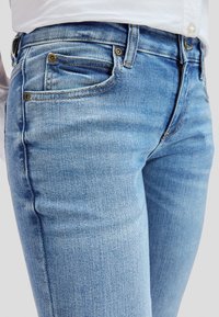 Artinimas vaizdas žmogaus, dėvinčio šviesiai mėlynas džinsines kelnes ir baltą marškinius, akcentuojant priekinius kišenės ir liemens sritį.