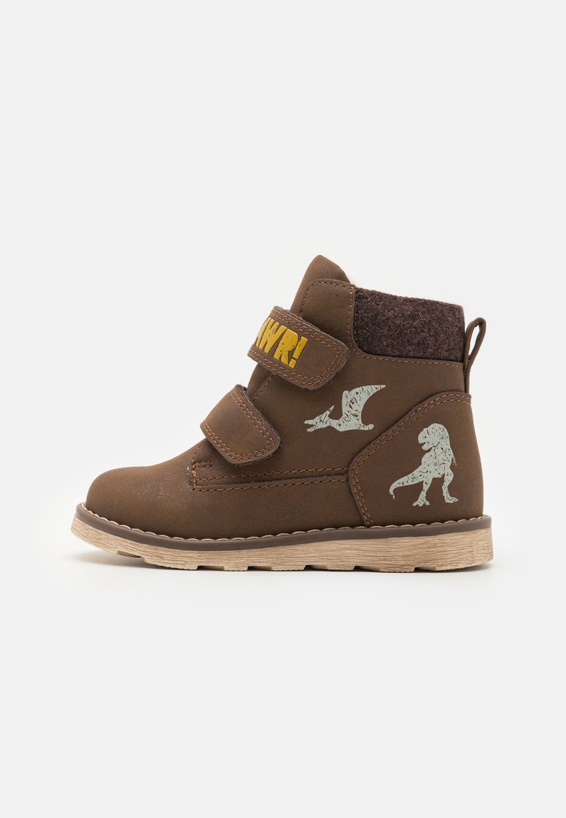 Bottes chelsea brunes avec deux bandes Velcro, présentant un dessus en feutre texturé et des graphiques de dinosaures. Semelle en caoutchouc léger et détails de couture.