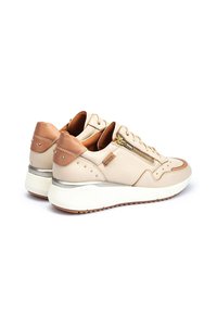 Zapatillas de cuero beige con acentos metálicos marrones, tachuelas decorativas y cremalleras laterales. Suela blanca con una sección gris claro. Forma redondeada.