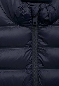 Námořnická puffy bunda s vysokým límcem, horizontálně prošívanou strukturou a centrálním zipem. Materiál vypadá hladce a mírně leskle.