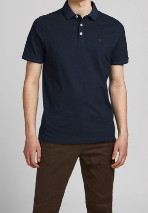 Dunkelblauses Polohemd mit einem Kragen, drei weißen Knöpfen und einem kleinen blauen Logo auf der linken Brust. Aus Baumwolle, mit kurzen Ärmeln.