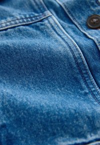 Közelkép kék farmeranyagból, részletes varrással és egy barna gombbal egy varrott varrással.