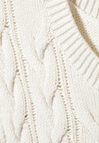 Fehér cable-knit pulóver, amely texturált mintával és kiemelkedő fonatokkal, valamint bordás szélekkel rendelkezik, vastag, kényelmes anyagból készült.