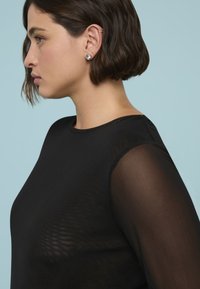 Schwarzes Oberteil mit einem einfarbigen Körper und durchscheinenden, semi-transparenten Ärmeln. Das Design umfasst einen Rundhalsausschnitt und eine glatte Textur.