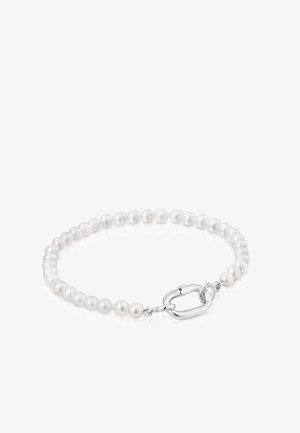 Brazalete con pequeñas perlas redondas blancas y un cierre de langosta plateado sobre una superficie reflectante blanca.