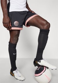 Mustat jalkapallosortsit, joissa on vaaleanpunainen reunus ja Paris-logo. Mustat kompressiosukat ja valko-mustalla designilla varustetut Nike-jalkapallokengät täydentävät asun.