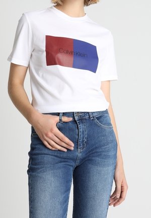 White cotton t-shirt featuring a red and blue rectangular graphic with "Calvin Klein" text in the center. Slim fit style, short sleeves.