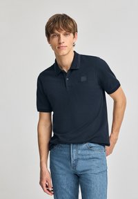 Polo de marina de manga corta, con collar y un pequeño parche de logo, combinado con jeans de pierna recta de color azul claro. Tejido de algodón suave.