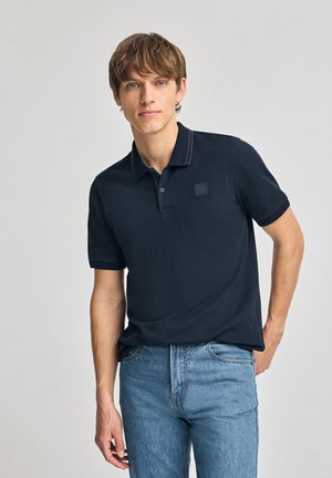 Polo de marina de manga corta, con collar y un pequeño parche de logo, combinado con jeans de pierna recta de color azul claro. Tejido de algodón suave.