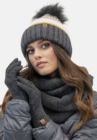 Gray knitted beanie with a pom-pom, white and yellow stripes, matched with gray gloves and a textured gray scarf, all in warm materials.