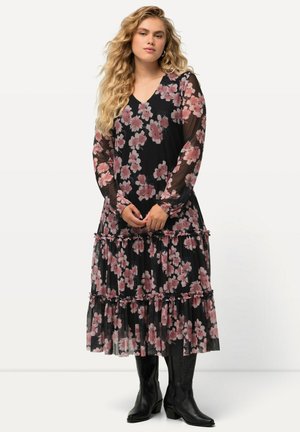 Lang zwart bloemenjurk met roze bloemen, gerimpelde lagen en transparante lange mouwen. Gecombineerd met zwarte cowboylaarzen. V-hals ontwerp.