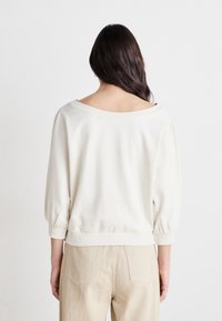 Crème-kleurige pullover sweatshirt met een brede halslijn, driekwart mouwen en een aangesloten tailleband, gecombineerd met beige broek.