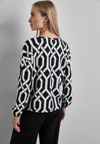 Schwarzer und weiß gemusterter Pullover mit geometrischem Design, langen Ärmeln und elastischen Bündchen. Der Stoff wirkt weich mit einer leichten Textur.