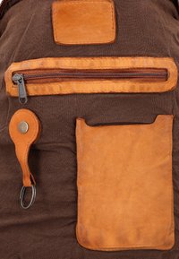 Brown fabric surface with tan leather patch, zippered pocket, key holder with metal ring, and rectangular leather pouch attached.