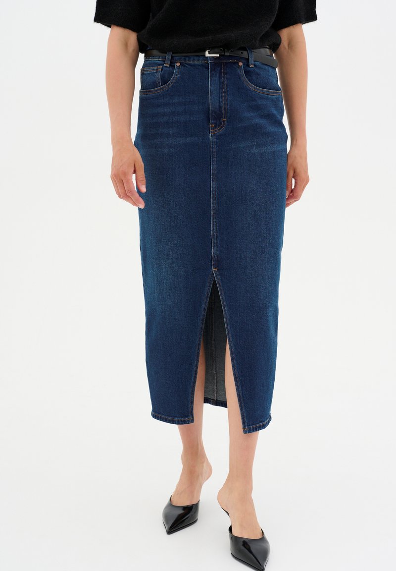 Sötétkék denim midi szoknya elöl hasítékkal, öt zsebes kialakítással és varrott részletekkel. Fekete, hegyes orrú magassarkú cipővel párosítva.