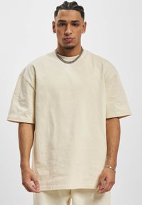 Light beige oversized t-shirt with short sleeves, made from soft cotton material. Features a round neckline and smooth texture.