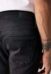 Jeanși negri din denim, cu o textură netedă, design cu cinci buzunare și o etichetă din piele cu "ANTONY MORATO" la talie.