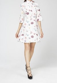 Blommig klänning med hög krage, trekvartslånga ärmar och utsvängd nederdel; har pastellfärgade rosa, lila och blå blommor på vit botten.