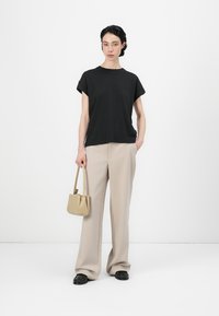 Svart t-shirt med kort ärm kombinerad med beige vida byxor. Modellen håller en liten beige handväska och bär strukturerade svarta skor.