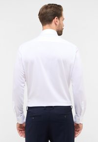 Wit langemouw shirt met een puntige kraag, gladde stof en geknoopte manchetten, gedragen met marineblauwe broek met dubbele achterzakken.