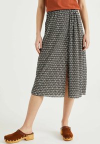 Black and white patterned midi skirt with a front slit, made of lightweight fabric. Worn with brown clogs featuring wooden heels and metal accents.