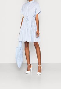 Nieprawidłowości w niebieskiej sukience w paski z ściągaczem w talii, krótkimi rękawami i warstwową spódnicą. Połączona z białymi butami na wysokim obcasie i dopasowaną torebką.