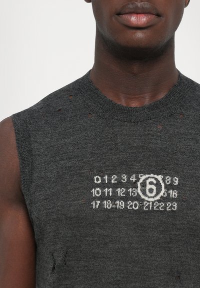 Primo piano di una persona che indossa un top a maglia senza maniche di colore grigio scuro con piccoli fori e numeri bianchi da 0 a 23, con il numero 6 cerchiato al centro.