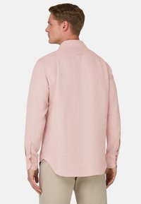 Camicetta rosa chiaro a maniche lunghe realizzata in un tessuto testurizzato. Presenta un colletto a punta e polsini con bottoni, con un orlo arrotondato.