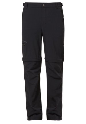 Hombre con camisa de manga larga gris oscuro, pantalones cargo negros y botas de senderismo marrones de pie sobre un fondo liso y claro.