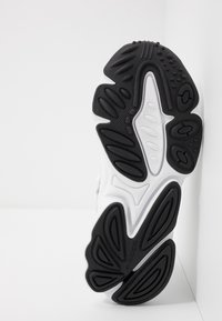 Suela de zapatilla en blanco y negro con goma texturada, que presenta un diseño ondulado y patrones de relieve pronunciados para mayor tracción.