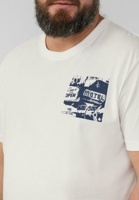 White cotton T-shirt featuring a navy graphic print on the left chest with vintage motel imagery and text "Come in, we’re OPEN."