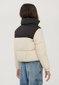 Beżowa i czarna kurtka puchowa z wysokim kołnierzem, z pikowanym wzorem, elastycznymi mankietami i skróconą sylwetką. Widok z tyłu.