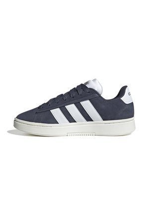 Sneaker en daim bleu marine avec des accents de rayures blanches, présentant un bout rond, un laçage et une semelle en caoutchouc blanc avec une texture antidérapante.