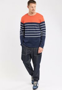 T-shirt à manches longues orange et marine, avec des rayures blanches horizontales. Porté avec un jean bleu foncé à coupe ample et des baskets bleues.