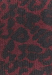 Texturerad tyg i mörkröd med ett svart leopardmönster, med en ribbad yta för extra djup och visuell intresse.