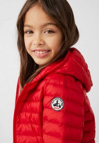 Rode donzen jas met een doorgestikt ontwerp, voorzien van een capuchon en een ronde patch-logo op de linkermouw. Gladde, glanzende textuur.