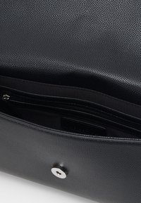 Sac en cuir noir texturé avec fermeture à pression magnétique, comportant une poche zippée intérieure et une doublure lisse.