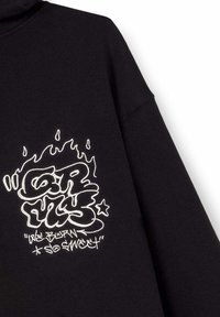 Felpa nera con grafica testuale in stile graffiti bianco. Tessuto morbido con una vestibilità comoda. I dettagli includono accenti simili a fiamme sopra il testo.